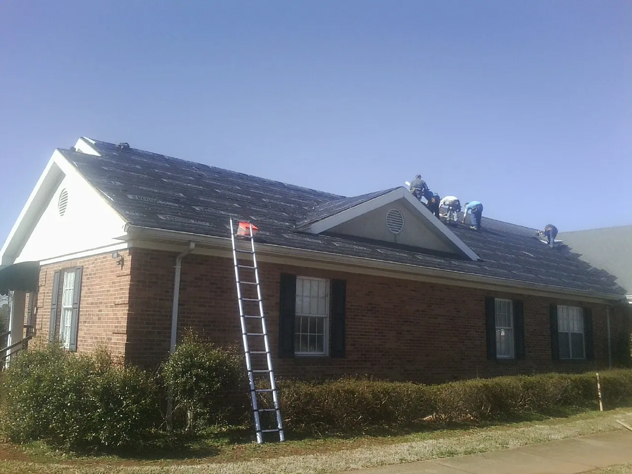 Crew tearing shingles off a brick ranch roof with a ladder set — Metal Roof Repair work by our crew in Mickleton