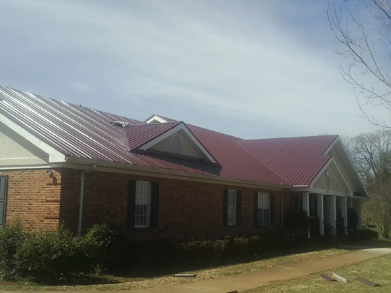 Red metal roof with gabled entries on a long brick building, from a Hail Damage Roof Repair job in Mickleton