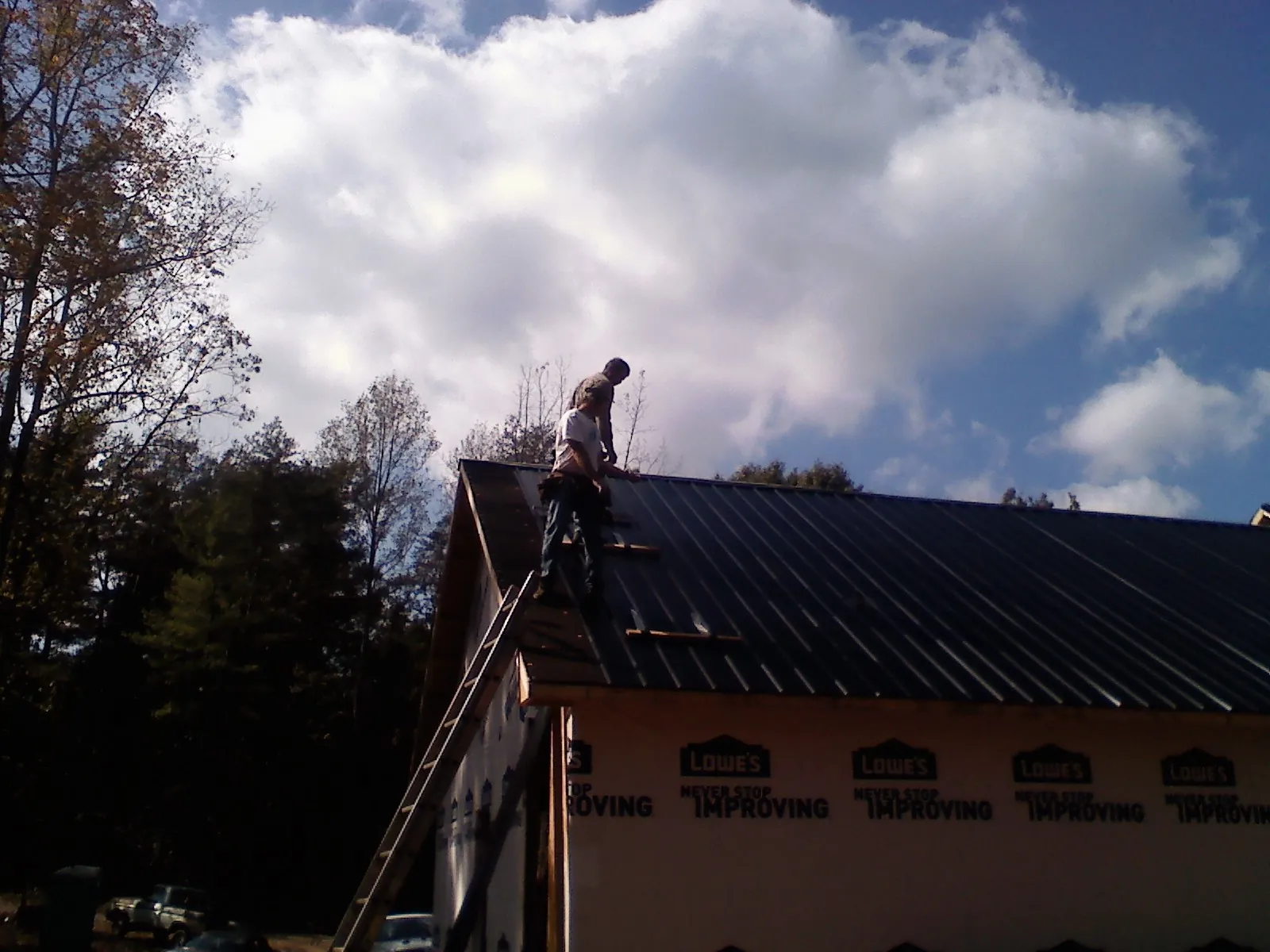 Roofer fastening dark metal panels high against a cloudy sky, from a Roof Inspection job in Mickleton